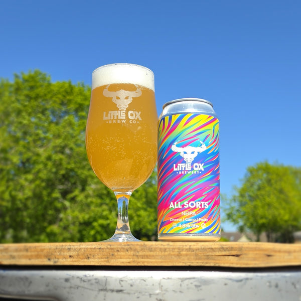 Beer glass and can with 'Little Ox Brewery' branding against a blue sky and green trees background